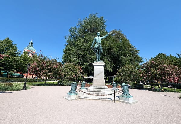 an open space in the King's garden park in Stockholm. The is a large copper statue in the middle, and trees and flowers on the side.