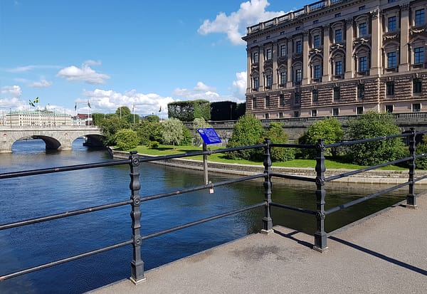 A photo of the Riksbron bridge in Stockholm. There is an imposing stone building to the right, water below, and a blue summer sky above.