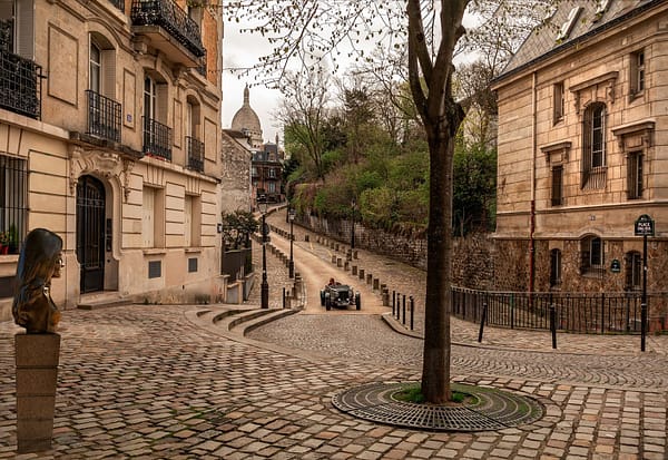 A photo of a cosy cobblestone street in Montmartre in Paris. Little stone houses are lining the street on both sides.