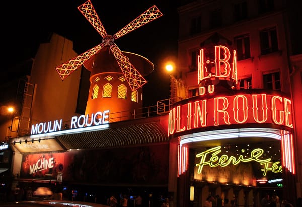 A night time photo of the Moulin Rouge in Paris, the bright neon signs illuminating the dark street.