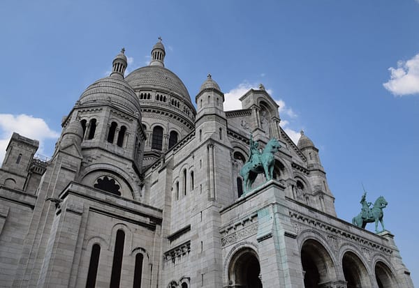 A photo of a part of th sacre ceur church in Paris. The white stone contrasting against a clear blue sky.