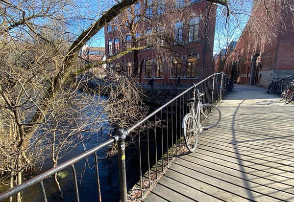 A photo of a small wooden bridge across the Akerselva river in Oslo. A bike is leaning against the bridge railing.