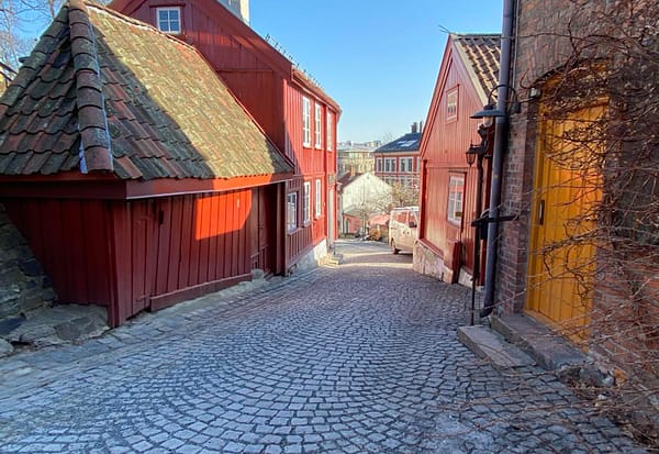 A photo of the old wooden houses at Damstredet in Oslo. Red houses are crowded along a narrow cobblestone street.