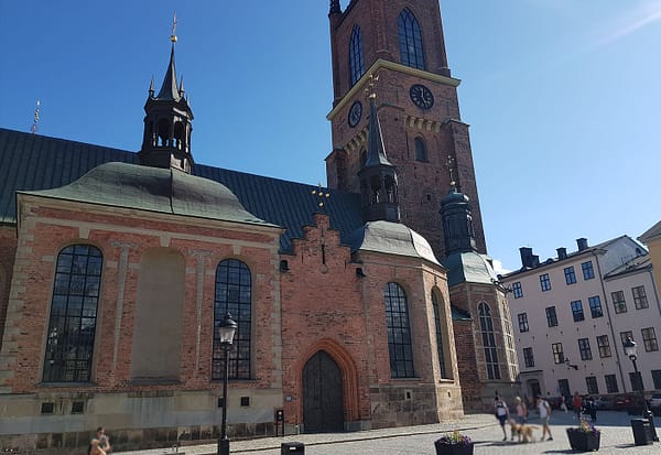 A photo of the Riddarholmen church in Stockholm. The church is a large, gothic, red brick building with green copper towers.