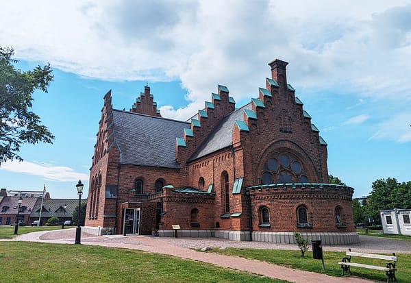 Ett foto av St Nicolai kyrka i Trelleborg. Kyrkan är i rött tegel, med trappgavlar. det är en fin sommardag med blå himmel och stackmoln.