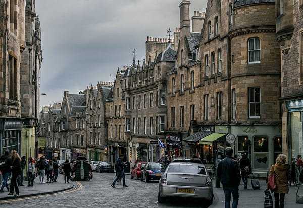 A photo of Cockburn street in Edinburgh on a grey day. People are rushing across a busy street.