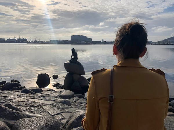 A woman in a yellow coat is looking at The Little Mermaid statue