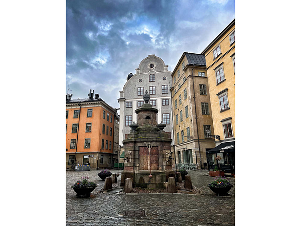 A photo of the old well at Stortorget in Stoclholm Old town. The backdrop is of colorful houses and a gray sky.