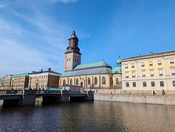 A photograph of one of the many canals in Gothenburg. A bridge is running across the water and on the other side is a large stone church with a green copper roof.