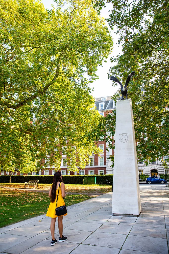 A young woman is standing in front of a large eagle monument in a park
