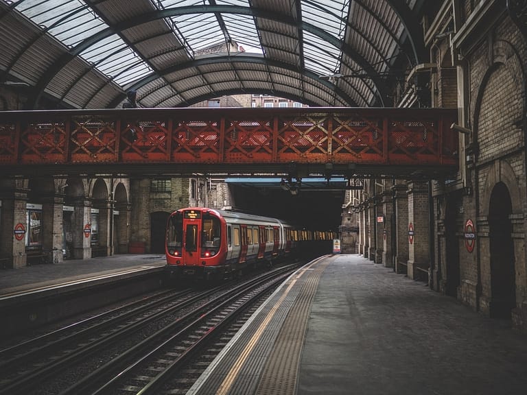 A train platform at Paddington station. A red train is waiting by the platform.
